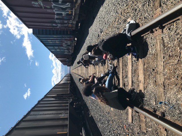 Students of Eva Carlston Academy sitting in empty train yard