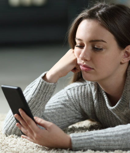 Teen lying on the floor looking at a smartphone, highlighting the need for a digital detox for teens