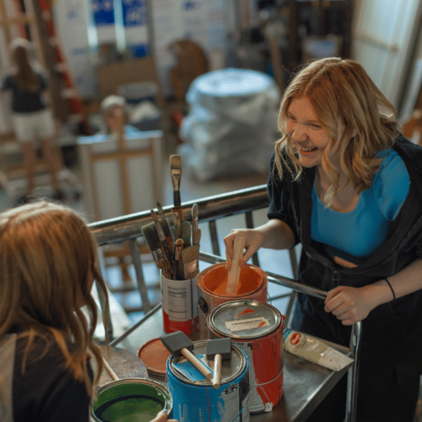 Creative Expression for Student Growth at Eva Carlston Academy: A student smiles while exploring painting techniques in the art studio, fostering joy and self-expression through hands-on creativity.