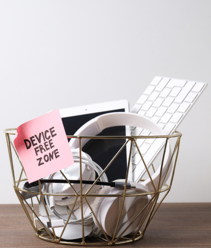 Basket labeled 'Device-Free Zone' holding headphones, a tablet, and a keyboard, symbolizing a digital detox for teens.