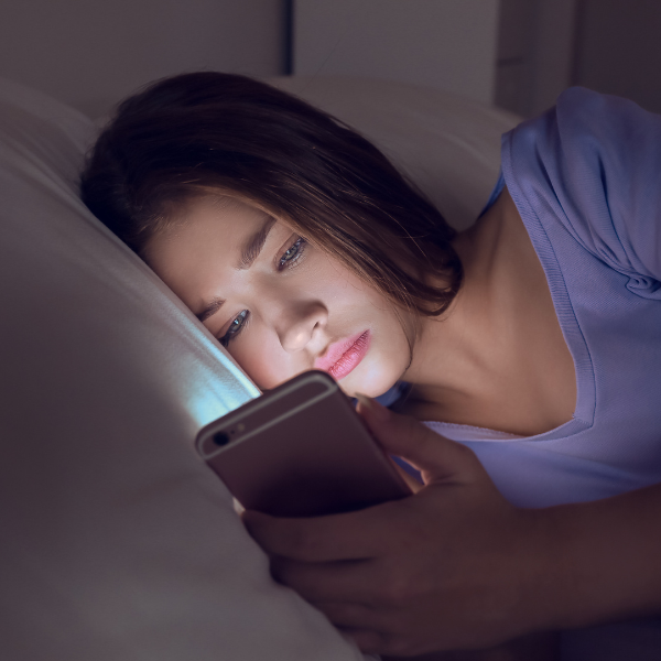 A teenage girl lying in bed at night, illuminated by her smartphone screen, symbolizing the need for a digital detox for teens to reduce late-night screen time.