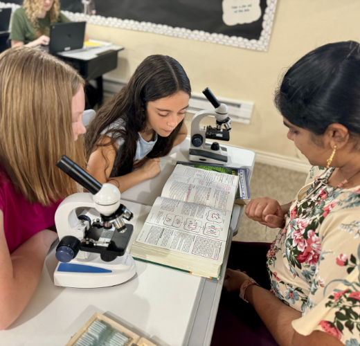 Students and a teacher engaging in a biology lesson with microscopes and textbooks, showcasing Critical Thinking at Eva Carlston Academy through hands-on learning and collaborative discussion.