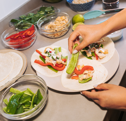 A person preparing healthy wraps with fresh vegetables, grilled chicken, and tortillas, demonstrating the role of nutrition in mental health through meal preparation.