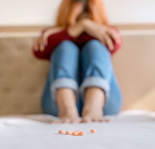 A distressed teen sitting on a bed with pills in the foreground, highlighting the impact of teen substance abuse and mental health myths.