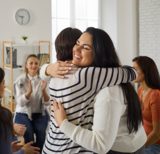 A supportive group therapy session where two women hug, symbolizing connection and recovery while addressing teen substance abuse and mental health myths.