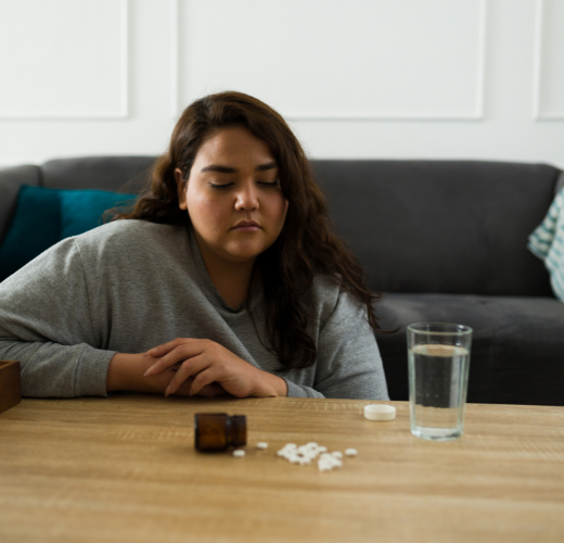 A teenage girl sitting by a table with pills in front of her, symbolizing the challenges of teen substance abuse and mental health myths.