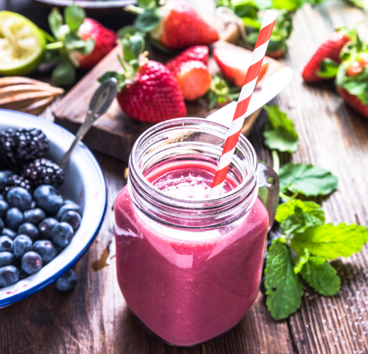 A vibrant berry smoothie in a mason jar with a striped straw, surrounded by fresh fruits like strawberries, blueberries, and blackberries, representing the role of nutrition in mental health through balanced and nutritious food choices.