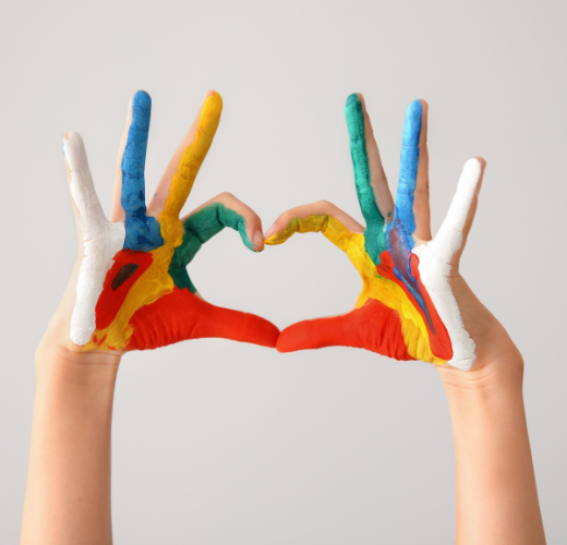 Two hands painted in bright colors forming a heart shape, reflecting the playful, expressive side of experiential learning at Eva Carlston.