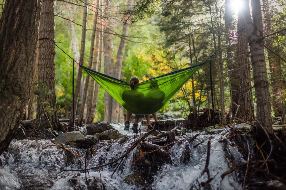 A teen sits in a bright green hammock above a creek surrounded by pine trees, reflecting the therapeutic opportunities in Utah found in nature.
