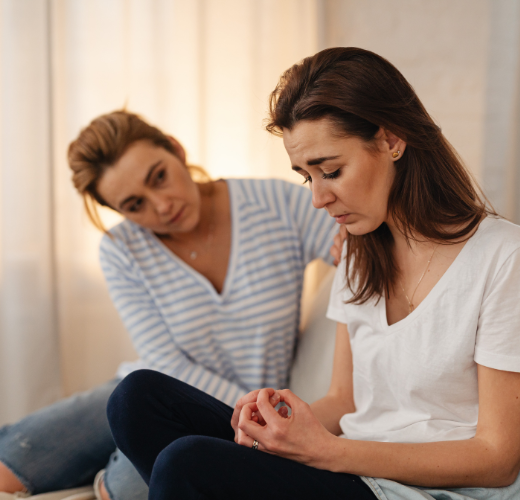 A supportive moment between two women indoors, with one offering comfort to the other, illustrating healing from PTSD through connection and trusted relationships.