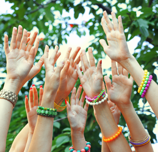 Group of raised hands adorned with colorful bracelets, symbolizing connection and community during The Summer Social Shift: Navigating Changing Friendships.